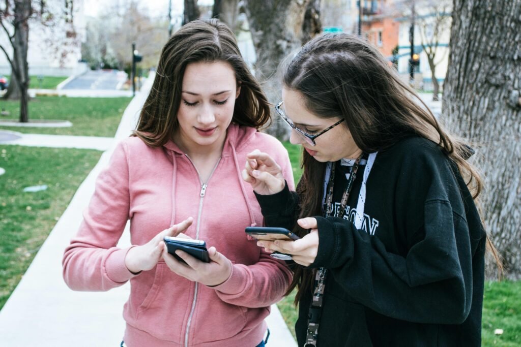 Two young women using smartphones outdoors, sharing information.
