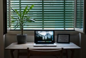 Elegant home office desk setup with a laptop and a plant near a window. Ideal for remote work.
